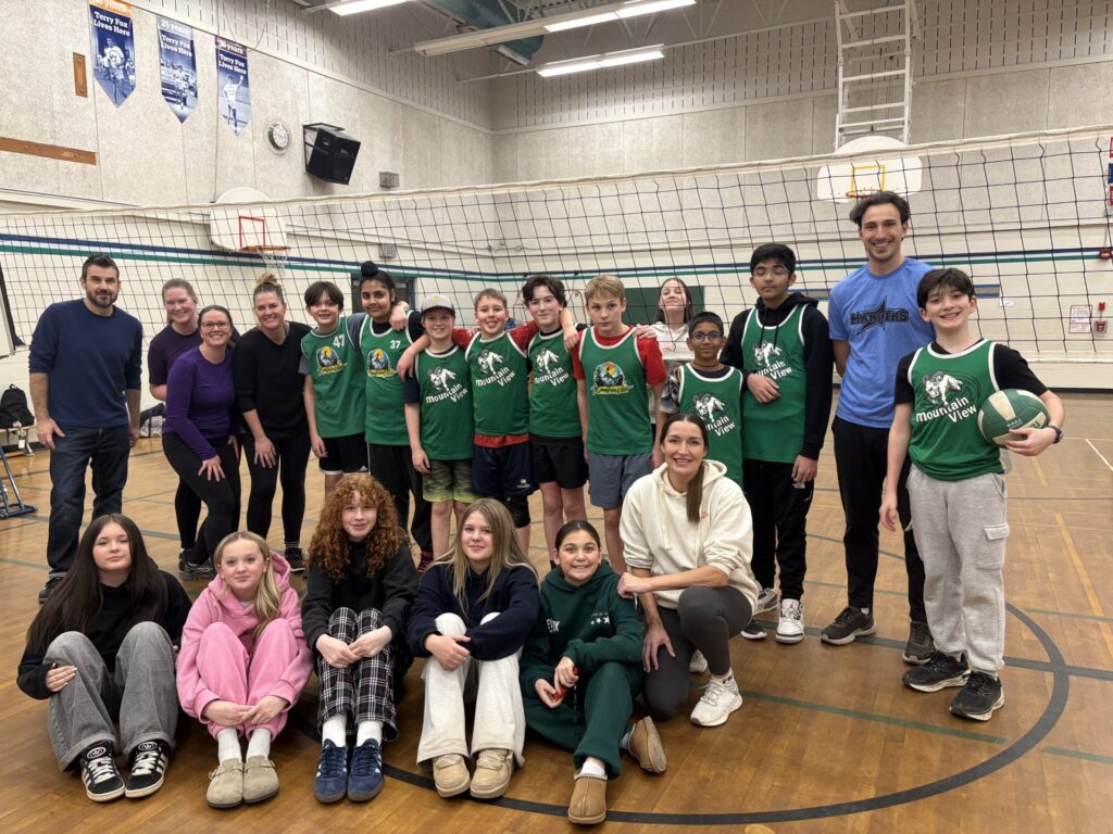 A young girl in a white dress writes at a desk surrounded by school supplies and a recycling poster.